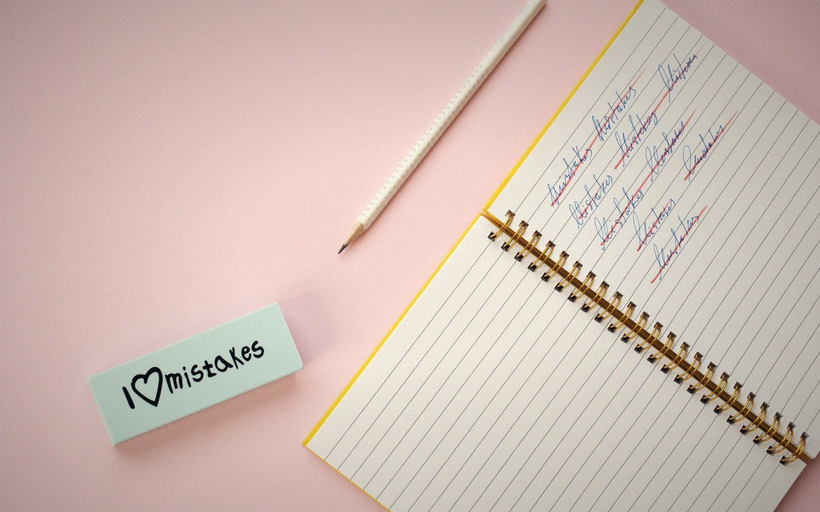 A pencil and eraser labeled "I love mistakes" beside a notebook of handwritten practice words
