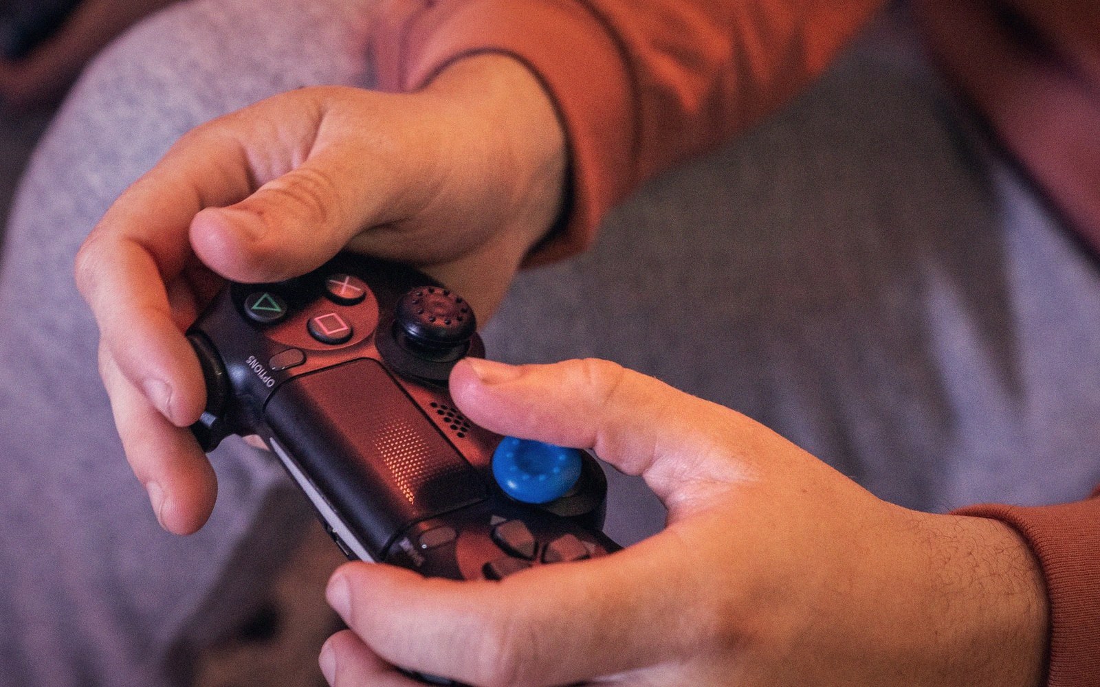 Close-up of hands gripping a PlayStation controller with a blue analog stick