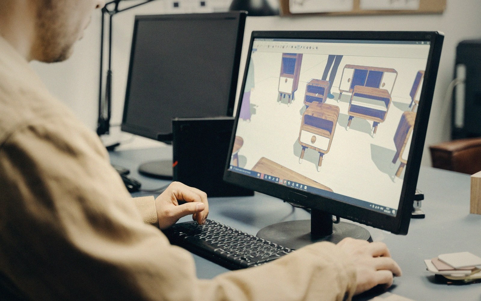 A designer views 3D furniture models on a computer screen while typing on a keyboard