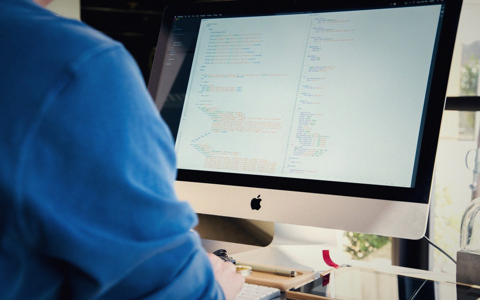 Person in a blue sweater viewing lines of code on an iMac screen
