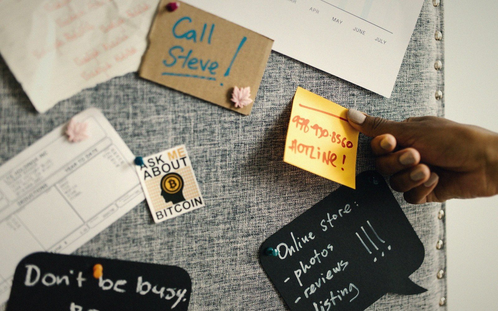 A hand pins a hotline note to a corkboard covered with reminders and sticky notes